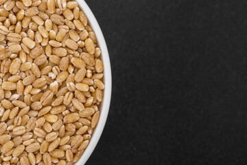 White glass bowl of pearl barley. Isolated on a dark grey background.
