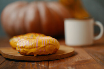 Sweet doughnuts with lemon glaze on a wooden tray. A large round pumpkin and a white mug on the background. Doughnuts with sprinkles.