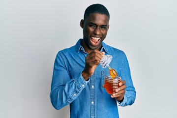 Fototapeta premium Young african american man holding honey smiling and laughing hard out loud because funny crazy joke.
