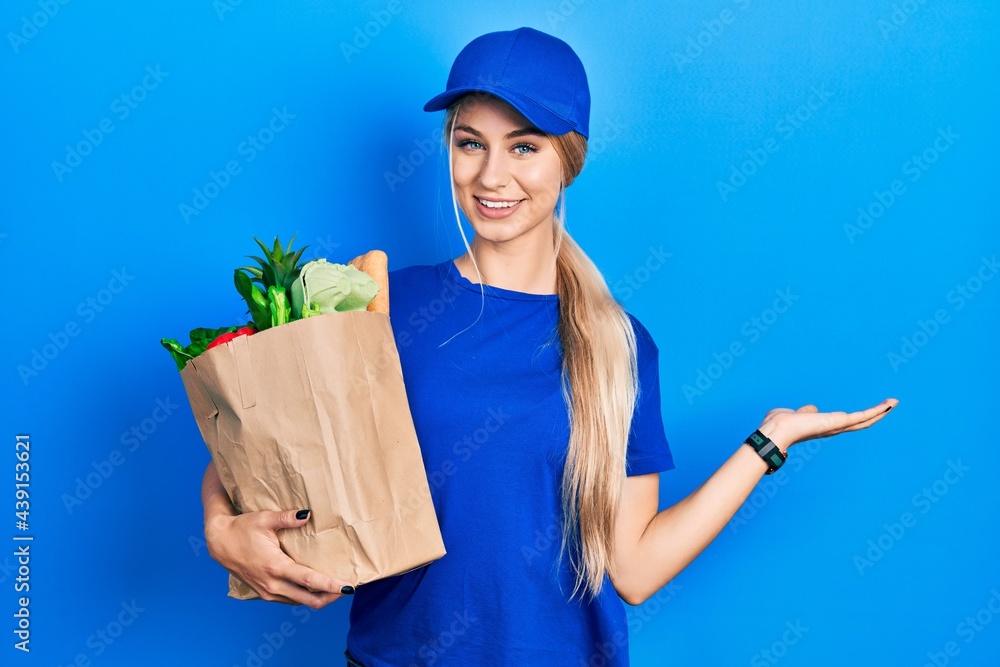 Canvas Prints young caucasian woman wearing courier uniform with groceries from supermarket smiling cheerful prese