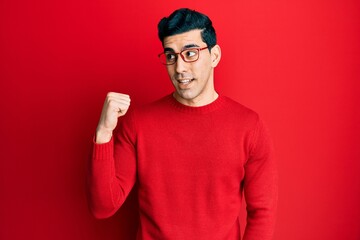 Handsome hispanic man wearing casual clothes and glasses pointing thumb up to the side smiling happy with open mouth