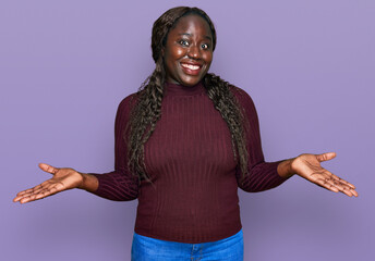 Young african woman wearing casual winter sweater clueless and confused expression with arms and...