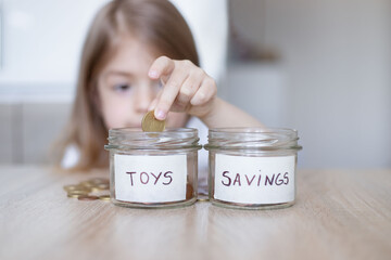 little girl is putting coin in glass jar for saving money. Focus on glass jar.