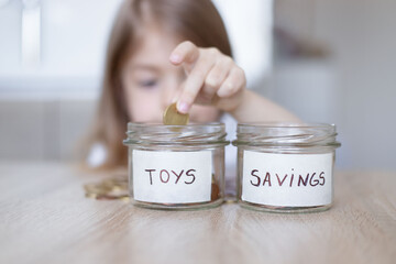 little girl is putting coin in glass jar for saving money. Focus on glass jar.