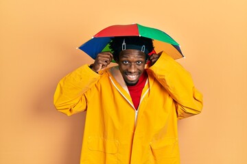 Young african american man wearing yellow raincoat smiling pulling ears with fingers, funny gesture. audition problem
