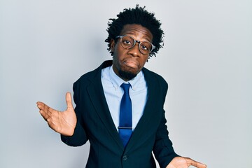 Young african american man wearing business suit clueless and confused expression with arms and hands raised. doubt concept.