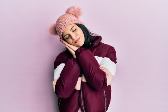 Young hispanic woman wearing wool winter sweater and cap sleeping tired dreaming and posing with hands together while smiling with closed eyes.