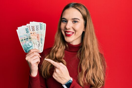 Young blonde woman holding czech koruna banknotes smiling happy pointing with hand and finger