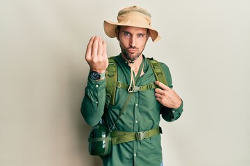 Handsome man with beard wearing explorer hat and backpack doing italian gesture with hand and fingers confident expression