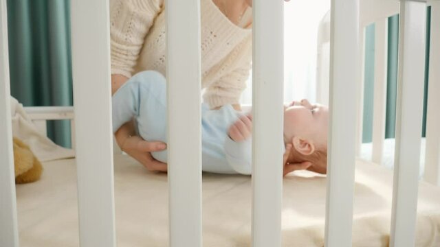 Young mother laying her little baby son in wooden cradle. Concept of parenting, family happy lifestyle and baby development