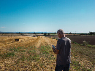Farmer watching the mobile phone in the field with tractor packing the cereal straw,