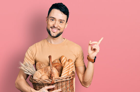 Hispanic man with beard holding wicker basket with bread smiling happy pointing with hand and finger to the side