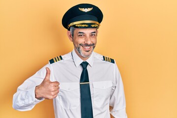 Handsome middle age man with grey hair wearing airplane pilot uniform doing happy thumbs up gesture...
