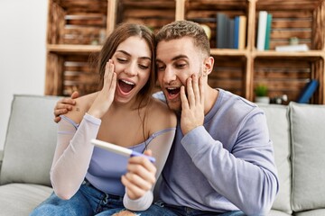 Young caucasian couple surprised looking pregnant test result at home.