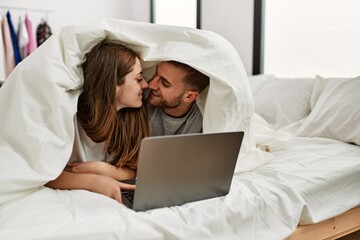 Young caucasian couple watching movie using laptop lying in bed.