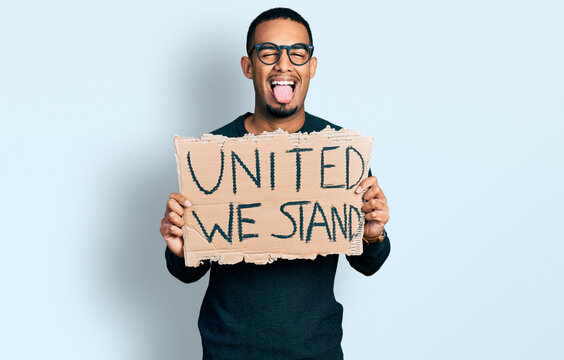 Young African American Man Holding United We Stand Banner Sticking Tongue Out Happy With Funny Expression.