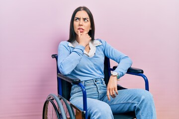Beautiful woman with blue eyes sitting on wheelchair thinking worried about a question, concerned...