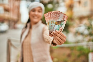 Young latin woman smiling happy holding new zealand dollars at the city.