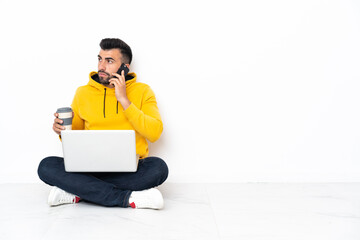 Caucasian man sitting on the floor with his laptop holding coffee to take away and a mobile