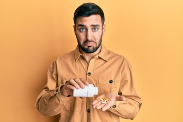 Young hispanic man holding pills depressed and worry for distress, crying angry and afraid. sad...