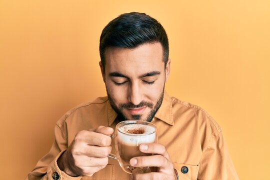 Handsome hispanic man enjoying a cup of coffee over yellow background