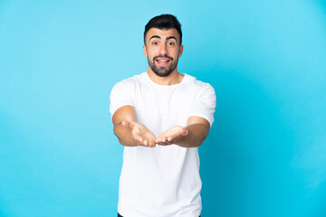 Caucasian man over isolated blue background holding copyspace imaginary on the palm to insert an ad
