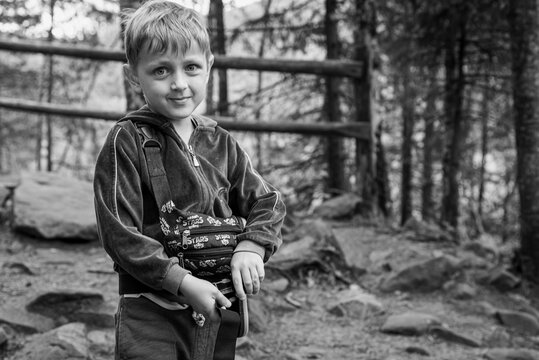 Little, cute boy smiling, walking in the mountains, forest on a sunny summer day. Black and white photo. Selective focus