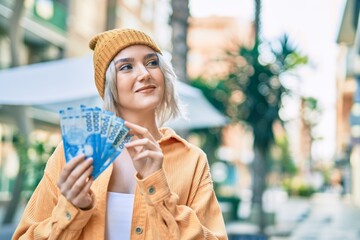 Young blonde girl smiling happy counting chilean pesos banknotes at the city.