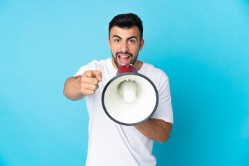 Caucasian man over isolated blue background shouting through a megaphone to announce something...