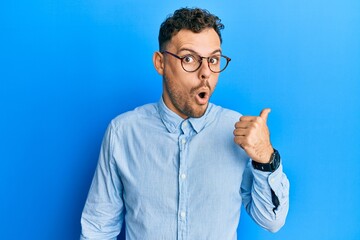 Young hispanic man wearing casual clothes and glasses surprised pointing with hand finger to the...