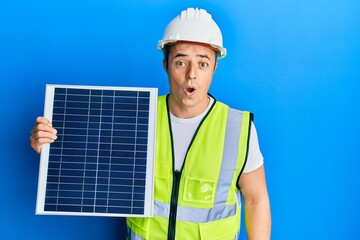 Handsome young man holding photovoltaic solar panel scared and amazed with open mouth for surprise, disbelief face