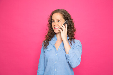 portrait color young redhead woman smiling talking on mobile phone with denim shirt on pink background