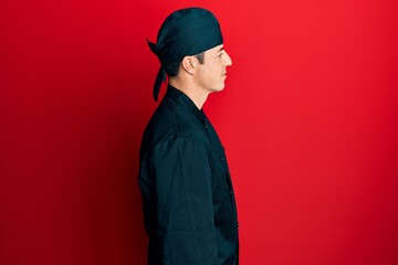 Fototapeta premium Handsome young man wearing professional cook uniform and hat looking to side, relax profile pose with natural face with confident smile.