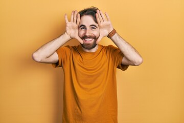 Caucasian man with beard wearing casual yellow t shirt smiling cheerful playing peek a boo with hands showing face. surprised and exited