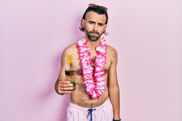 Young hispanic man wearing swimsuit and hawaiian lei drinking tropical cocktail depressed and worry...