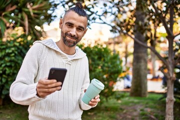 Fototapeta premium Handsome middle age man with beard standing happy and confident outdoors using smartphone