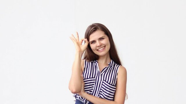 Attractive woman smiles at camera showing hand OK sign on white background. People lifestyle concept.