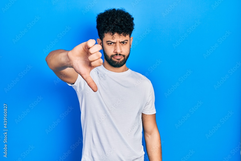 Wall mural young arab man with beard wearing casual white t shirt looking unhappy and angry showing rejection a