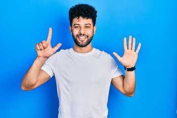 Young arab man with beard wearing casual white t shirt showing and pointing up with fingers number seven while smiling confident and happy.