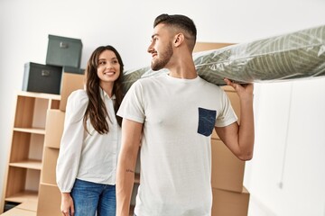 Young hispanic couple smiling happy holding carpet at new home.