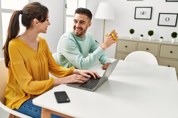 Young hispanic couple using laptop and smartphone drinking coffee at home.