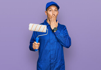 Bald man with beard holding roller painter covering mouth with hand, shocked and afraid for...