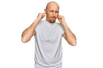 Fototapeta premium Bald man with beard wearing casual white t shirt covering ears with fingers with annoyed expression for the noise of loud music. deaf concept.