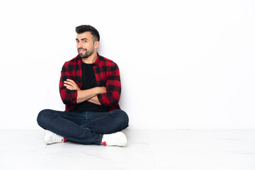 Young handsome man sitting on the floor with arms crossed and looking forward