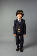 Boy dressed in a black pilot uniform stands at the gray background