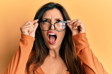 Beautiful hispanic woman wearing glasses angry and mad screaming frustrated and furious, shouting with anger looking up.