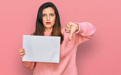 Beautiful hispanic woman holding blank empty banner with angry face, negative sign showing dislike...