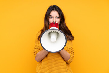 Young caucasian woman isolated on yellow background shouting through a megaphone