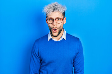 Young hispanic man with modern dyed hair wearing sweater and glasses afraid and shocked with surprise expression, fear and excited face.