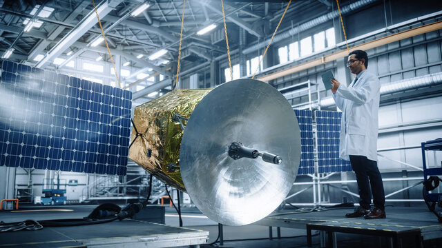 Male Engineer Uses Digital Tablet Computer while Working on Satellite Construction. Aerospace Agency: Scientist uses Augmented Reality Software for Building Spacecraft for Space Exploration